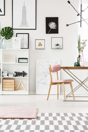Pink wooden chair at a table with plants in bright dining room interior with posters on the wall and...