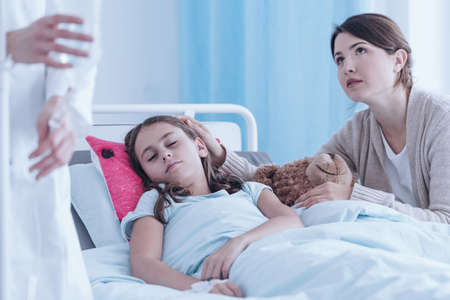 Worried mother supporting her daughter suffering from cancer in health centerの写真素材