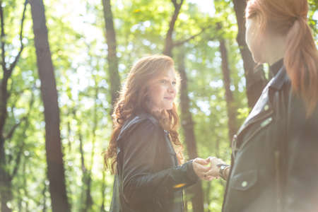 Low angle of red-haired girls holding hands in the forest during sunny day