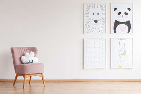 Pink armchair with cloud shaped toy standing in baby room with simple posters on empty wallの写真素材