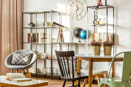 Heathers in gold pots on table with chairs next to cupboard with book in cozy living room interior with telescope on the shelfの写真素材