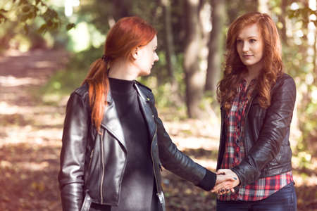 Red-haired girlfriends holding hands during a walk in the forest