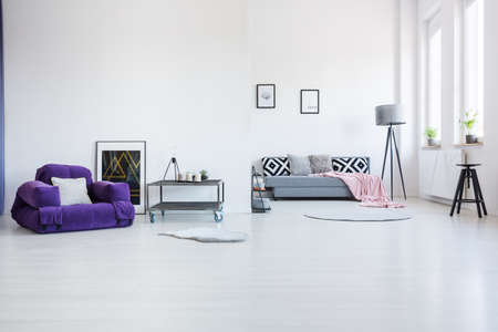 Purple armchair next to industrial table in spacious living room interior with black stool and patterned cushions on the sofaの写真素材