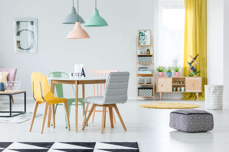 Patterned, black and white pouf in pastel dining room interior with colorful chairs standing at a wooden tableのeditorial素材