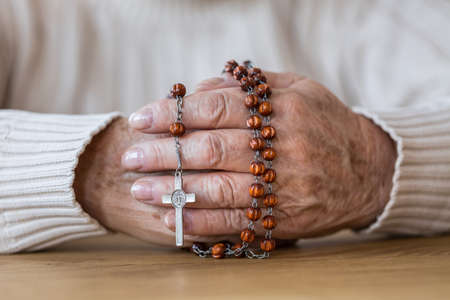 Close-up of senior's hands holding a red rosary with silver crossの写真素材