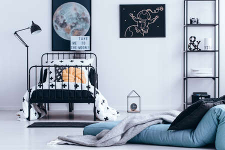 Blanket on blue mattress next to bed with pastel pillow in teenager's bedroom interior with moon and...