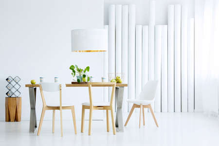 Green apples placed in metal basket standing on oak table in white dining room interior with plantの写真素材