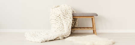Close-up of white knit blanket on wooden stool in cozy interior with fur rugの写真素材