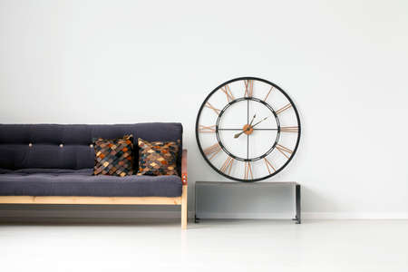 Gold, round clock on metal bench next to a black, wooden settee with brown cushions in living room interiorの写真素材