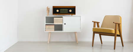 Close-up of yellow armchair next to white cupboard with vintage radio in simple bright interior