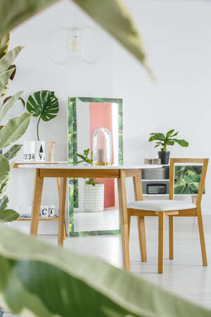 In the background wooden chair at table in dining room interior with leaf and mirror