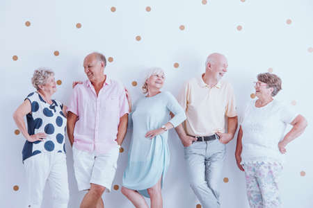 Happy elders leaning against white wall with dots and looking at each otherの写真素材
