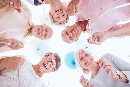 Group of smiling seniors looking down and holding balloonsの写真素材