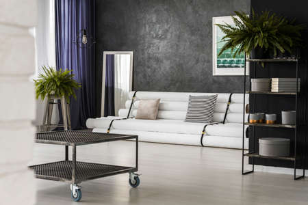 Mirror next to white settee in bright living room interior with industrial table and fernsの写真素材