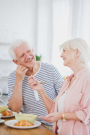 Happy senior couple smiling each other while eating breakfast