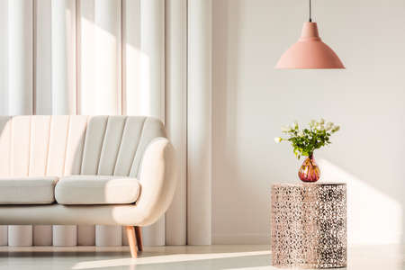 White, elegant sofa, pink lamp and flowers on metal table in a living room interiorの写真素材