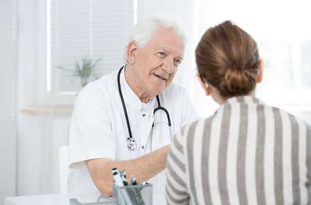 Senior doctor explaining the treatment to a female patient in white officeの写真素材