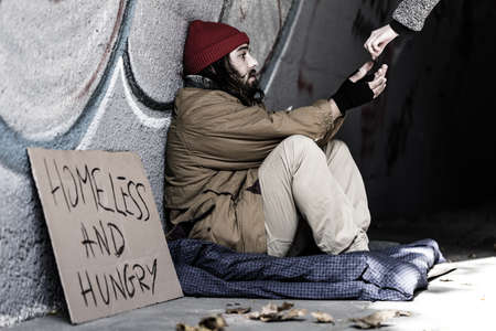Poor and hungry man sitting in the underground passage and accepting help
