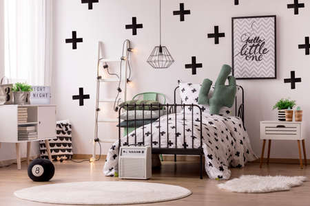 White round rug near bed with patterned blanket in scandinavian bedroom interior with poster and...