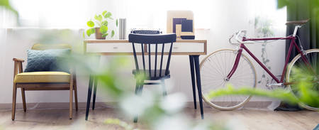 Red bicycle next to bright workspace with black chair, wooden desk and vintage typewriterの写真素材