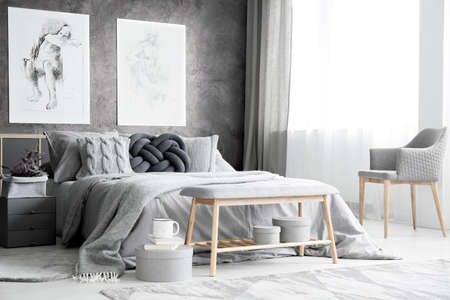Spacious bedroom with armchair, knot cushion on the bed and two posters hanging on textured wall