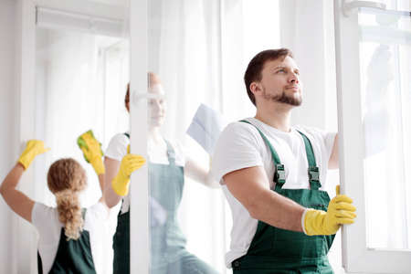 Cleaner in green overalls and yellow gloves washing windows in an apartmentの写真素材