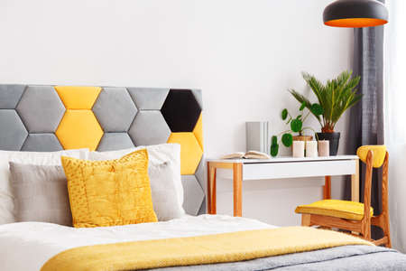 Close-up of colorful bed with hexagon bedhead in bright bedroom interior with yellow chair at wooden desk with plants and candlesの写真素材