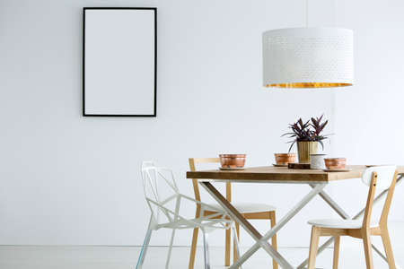 Mockup of empty poster in white dining room interior with lamp above wooden tableの写真素材