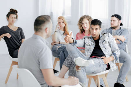 Teenage boy in denim jacket arguing with therapist during group psychotherapy