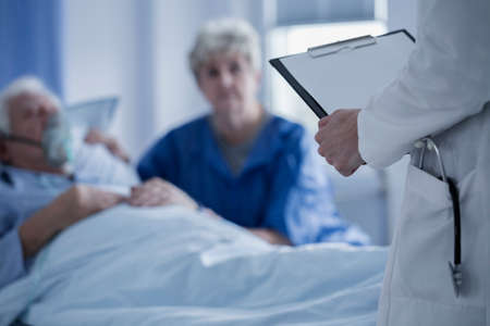 Doctor with stethoscope in the pocket of a white apron holding results of elderly patientの写真素材