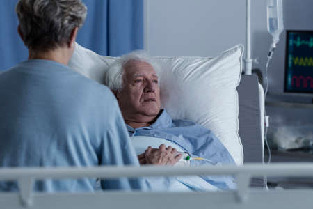 Worried wife visiting sick senior man with alzheimer connected to a drip in health centerの写真素材