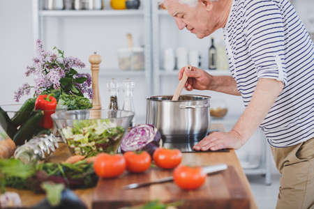 Elderly man smelling healthy tomato soup in the kitchen with vegetables