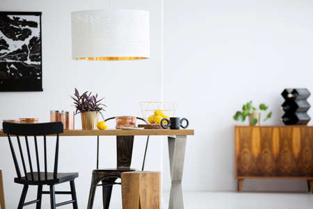 Black chairs at wooden table under white lamp in simple dining room interior with stoolの写真素材