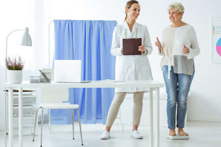 Senior happy woman standing on scales and checking diet progress during dietician consultationの写真素材