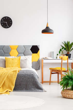 Plants in colorful bedroom interior with yellow blanket on gray bed standing next to a white desk with vintage, yellow chairの写真素材