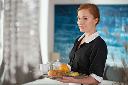 Smiling maid from room service holding a tray with food for breakfastの写真素材