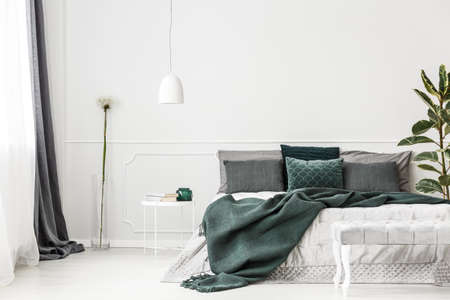 Emerald green bedding on bed with pillows against white wall with copy space in bedroom interiorの写真素材