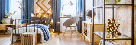 Close-up of black, metal rack with decorations in bedroom interior with wooden furniture and gray armchairの写真素材