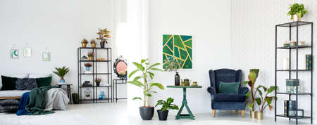 Table and armchair near plants in botanic living room interior with bed and paintingの写真素材