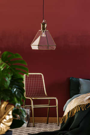 Lamp above green chair next to bed in red, luxurious bedroom interiorの写真素材