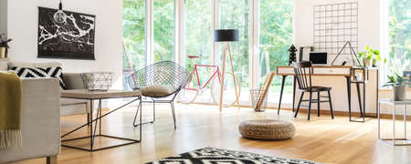 Basket on the table and pouf on the wooden floor in spacious living room with chair at desk, bike and lampの写真素材