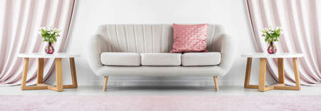 Cover photo of a beige sofa standing between two round tables with flowers in elegant living room interiorの写真素材