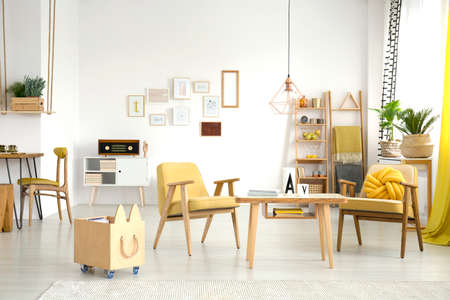 Copper lamp above wooden table standing between two yellow armchairs in cozy living room interiorの写真素材