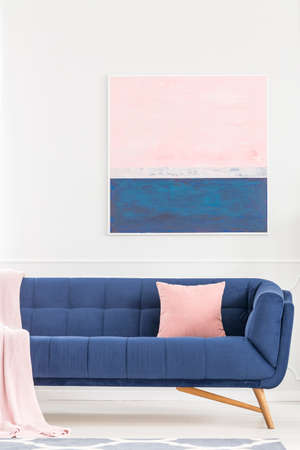Pink pillow on navy blue sofa against white wall with painting in pastel living room interiorの写真素材