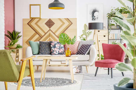 Patterned pillows on sofa next to red armchair in cozy living room interior with wooden furnitureの写真素材