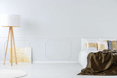 White wooden lamp and gold painting in elegant bedroom interior with dark bedding on bed