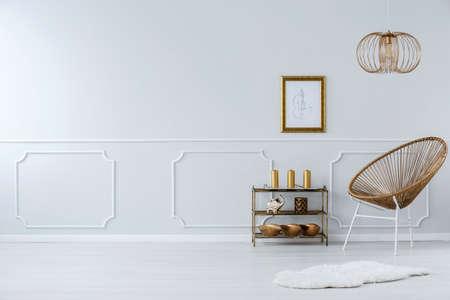 Lamp above gold chair and white fur in sophisticated living room interior with poster and copy spaceの写真素材