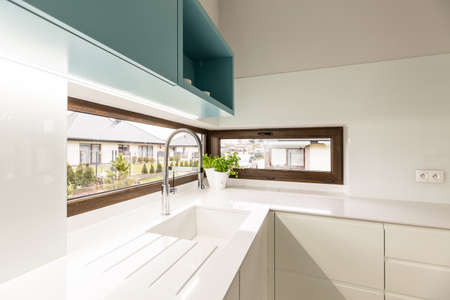 White sink in modern kitchen interior with blue cabinets and windows in houseの写真素材