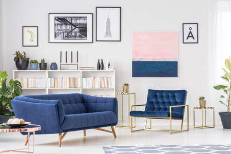 Navy blue sofa in sophisticated living room interior with armchair against the wall with gallery of...