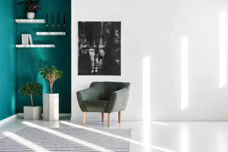 Grey armchair next to plants and black painting on the wall in a living room interiorの写真素材